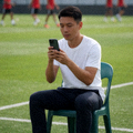 足球训练场边球迷使用手机查看比分的场景